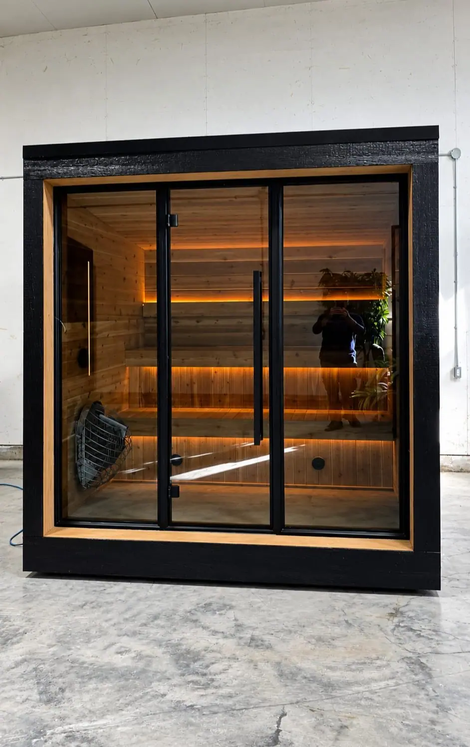 Black cube sauna with a three-panel glass front and lit benches
