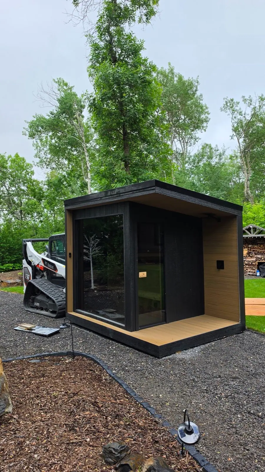Black cube sauna in a treed yard
